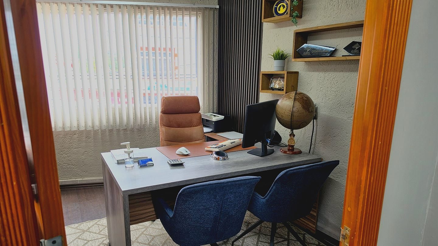 Oficina privada de GMG Contadores: escritorio con equipo de cómputo, sillón de piel, repisas con reconocimientos y ventanal con persianas